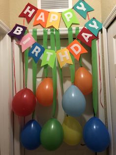 a birthday decoration with balloons and streamers hanging from the ceiling in front of a door