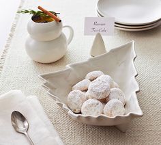 a bowl filled with powdered donuts on top of a table next to plates