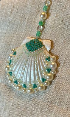 a necklace with pearls and green beads hanging from it's side on a piece of cloth