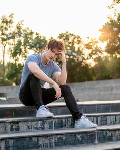 a young man is sitting on the steps and holding his hand to his face as he looks down