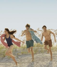 three young people running on the beach in swimsuits and one is holding a towel