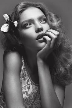 a black and white photo of a woman with flowers in her hair, posing for the camera