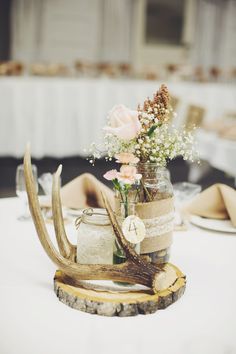 a vase filled with flowers and antlers on top of a white table cloth covered table