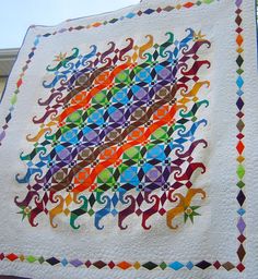 a multicolored quilt hanging on the side of a building with an intricate design