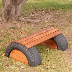 a wooden bench made out of old tires in the grass next to a large tree