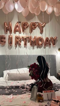 a woman is sitting on her bed with balloons and presents in front of her,