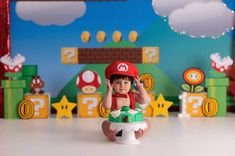 a little boy sitting on top of a table next to a nintendo game controller and mario mushroom figurine