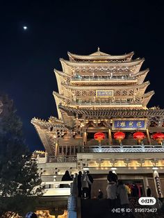 people standing in front of a tall building at night with the moon behind it and lights on