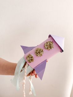 a person is holding a paper rocket with gold buttons on it and some white string