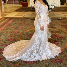 a woman in a white wedding dress standing on a carpeted floor with flowers behind her