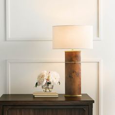 a table with a lamp and flowers on it next to a dresser in a room