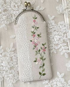 a white purse with pink flowers on it sitting on a lace covered tablecloth,