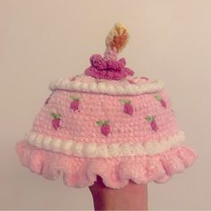 a crocheted pink hat with white trim and strawberries on the top is being held by a hand