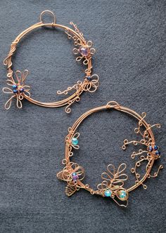 two gold hoop earrings with blue stones and filigrees on the ends, sitting on a gray surface