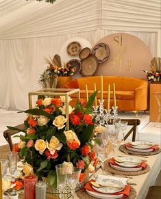 the table is set with orange and white flowers, candles, and place settings for dinner