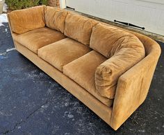 a brown couch sitting on top of a parking lot next to a garage door,