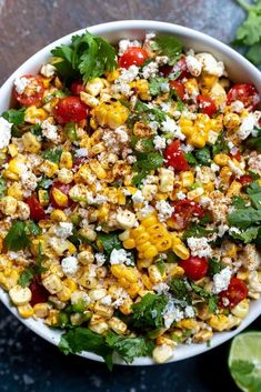 a white bowl filled with corn, tomatoes and feta cheese on top of lettuce