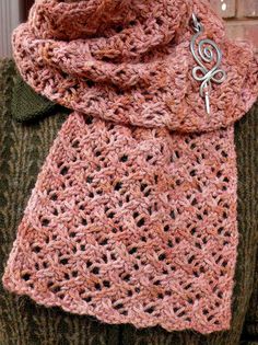 a woman wearing a pink crocheted scarf with a metal charm hanging from it