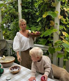 a woman standing next to a little boy at a table with food on top of it