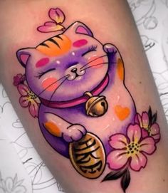 a cat tattoo on the leg with flowers around it and a bell in its paws