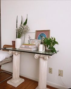 a glass table topped with books and plants next to a white bed in a room