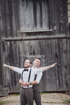 two men standing next to each other in front of a wooden building with their arms stretched out