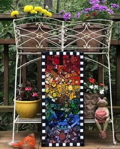 a colorful stained glass art piece sitting on top of a wooden bench next to potted plants