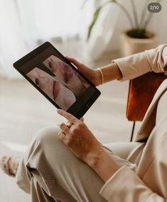 a woman sitting in a chair holding an electronic device with her face on the screen