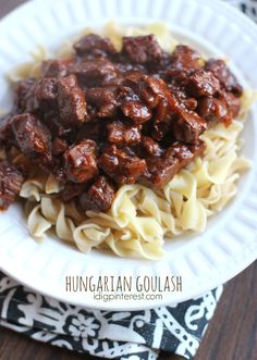 a white plate topped with pasta and meat covered in sauce on top of a wooden table