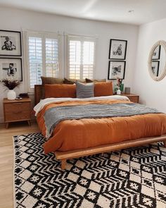 a bed with an orange comforter on top of it in a bedroom next to two windows