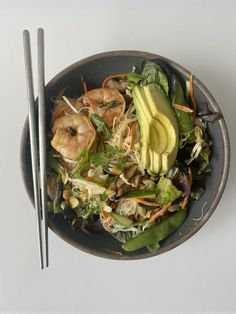 a salad with shrimp, lettuce and carrots in a bowl next to chopsticks