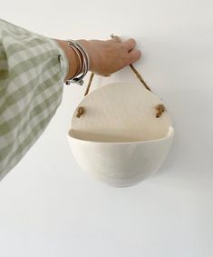 a person is holding a white bowl on a wall with string attached to it and hanging from the side