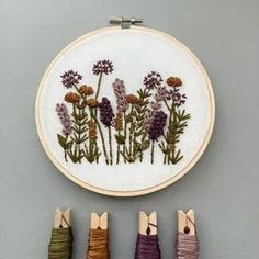 the embroidery is hanging on the wall next to five different colored yarns and needles