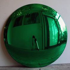 a green circular mirror sitting on top of a cement floor next to a white wall