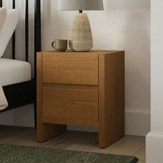 a nightstand with a lamp on top of it next to a bed