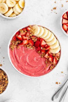 two bowls filled with fruit and granola on top of a white table next to spoons