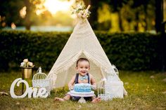 a baby sitting in front of a teepee with a cake