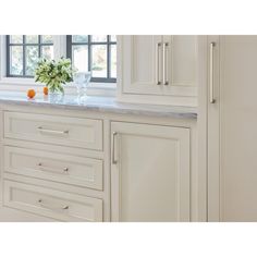 a kitchen with white cabinetry and marble counter tops, along with a vase filled with flowers