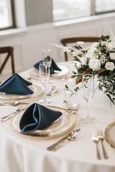 the table is set with white flowers and blue napkins, silverware and wine glasses