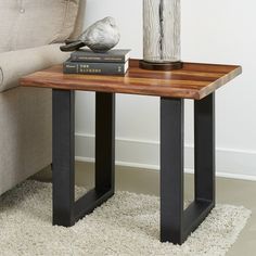 a bird sitting on top of a wooden table next to a book and glass vase