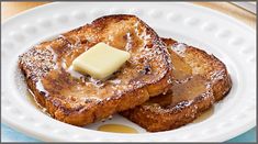 two pieces of french toast with butter on top and syrup on the side sitting on a white plate