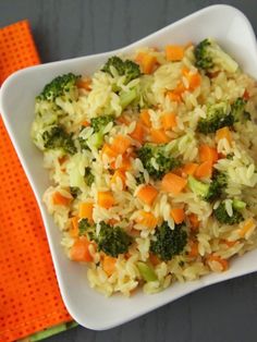 a white plate topped with rice and veggies next to a fork on an orange napkin