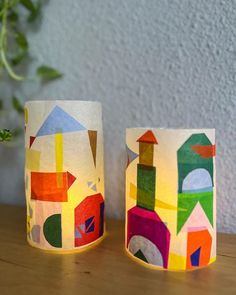 two paper cups sitting on top of a wooden table next to a potted plant