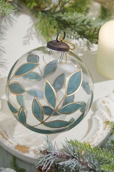 a glass ornament hanging from a christmas tree with evergreen branches and candles in the background