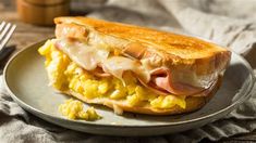 a sandwich with ham and eggs on a plate next to a fork, knife and napkin