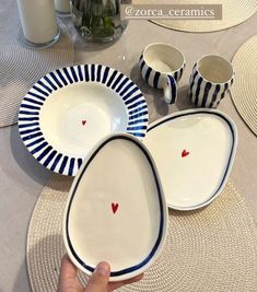 a hand is pointing at plates and cups on a table with place mats around them