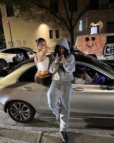 two people standing in front of a silver car