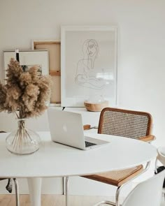 a white table topped with a laptop computer next to a vase filled with dried flowers