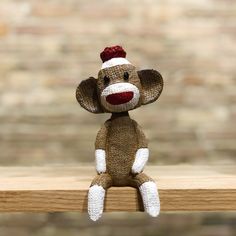 a small stuffed monkey sitting on top of a wooden table next to a brick wall