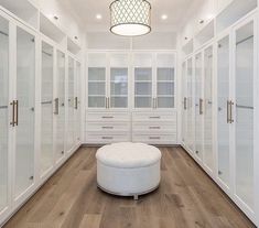 a large white closet with lots of drawers and glass doors on the walls, along with a round footstool